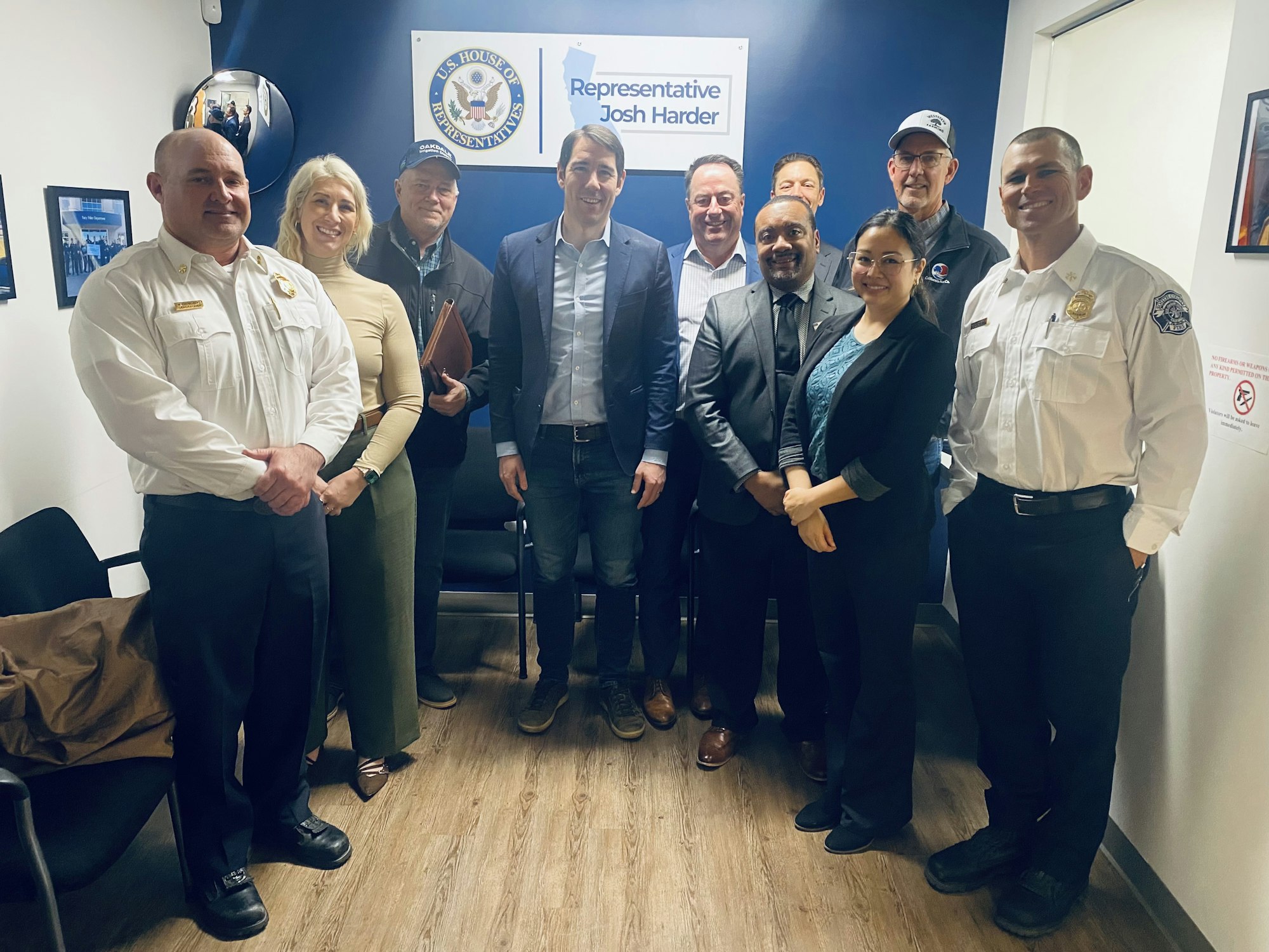 A group of people, including officials and representatives, pose for a photo in an office setting.