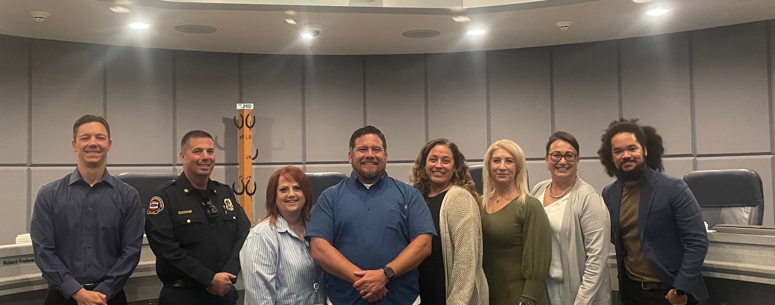 Group of people smiling in a semi-circular council chamber.