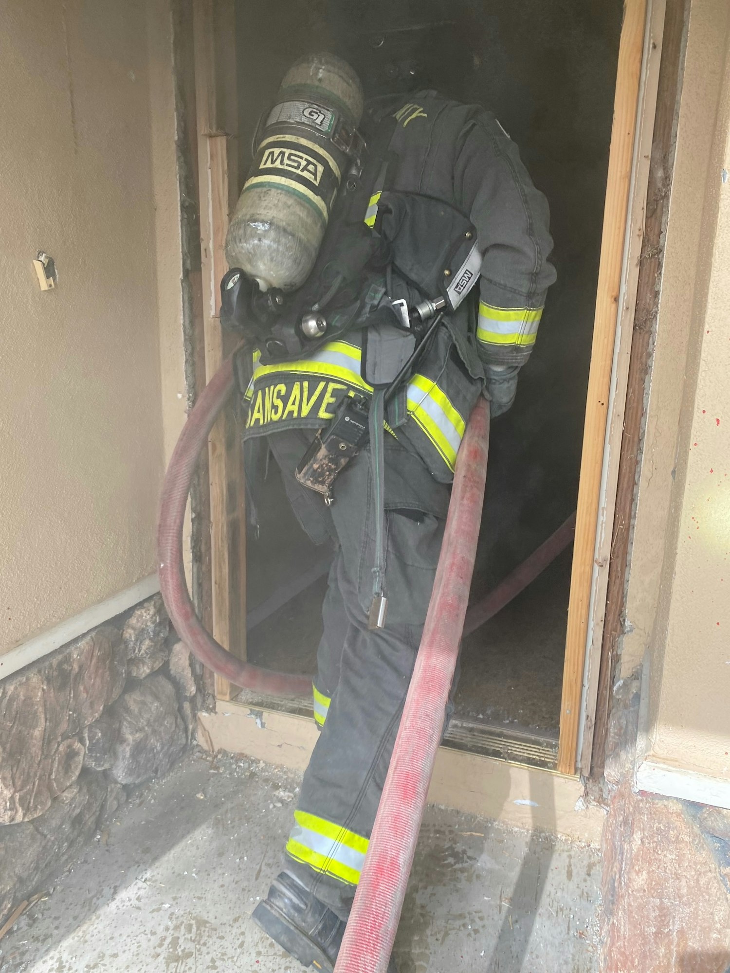 A firefighter in gear, entering a smoky area while carrying a fire hose, preparing to tackle a blaze.