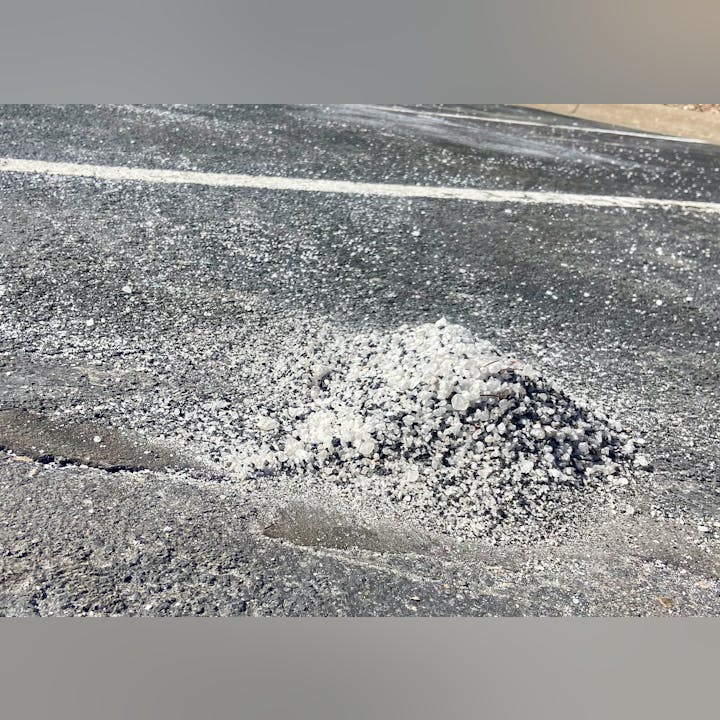 A pile of salt or grit on an asphalt surface, likely for de-icing or traction enhancement.