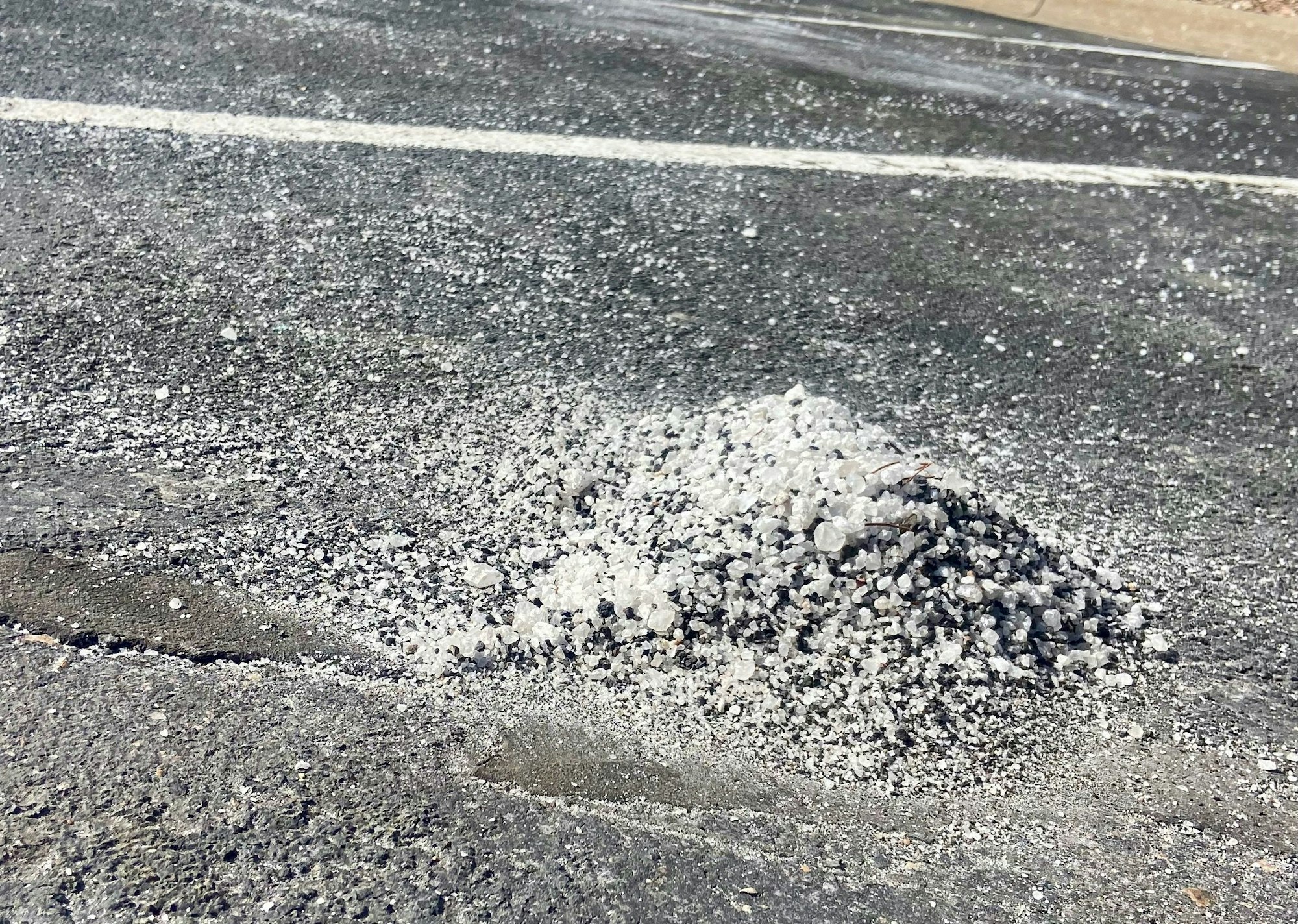 A pile of salt or grit on an asphalt surface, likely for de-icing or traction enhancement.