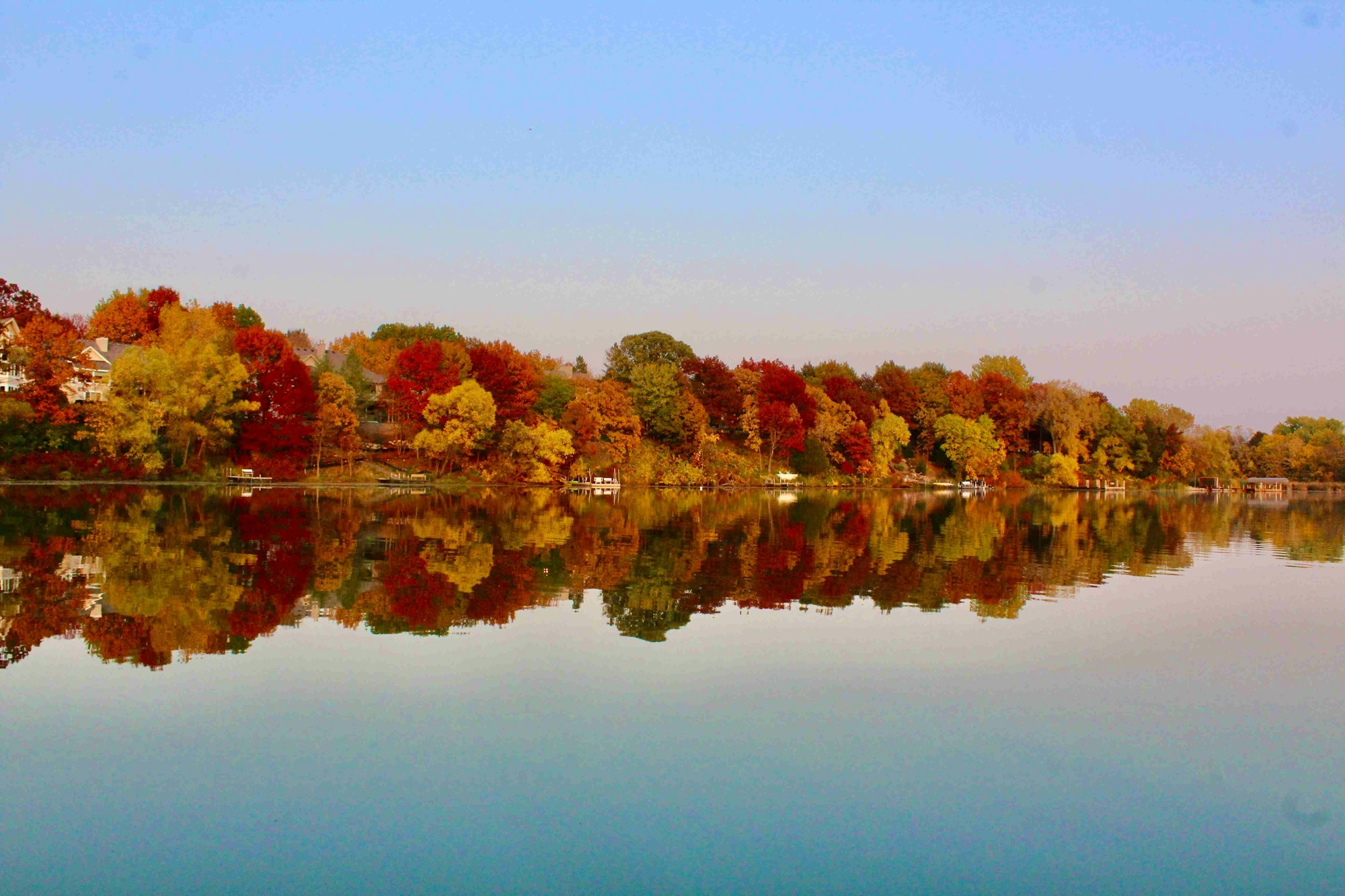 Autumn-colored trees reflecting on a calm lake under a clear sky.