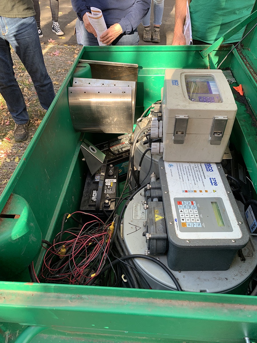 An open bin with electrical or mechanical equipment and wires, surrounded by people standing.