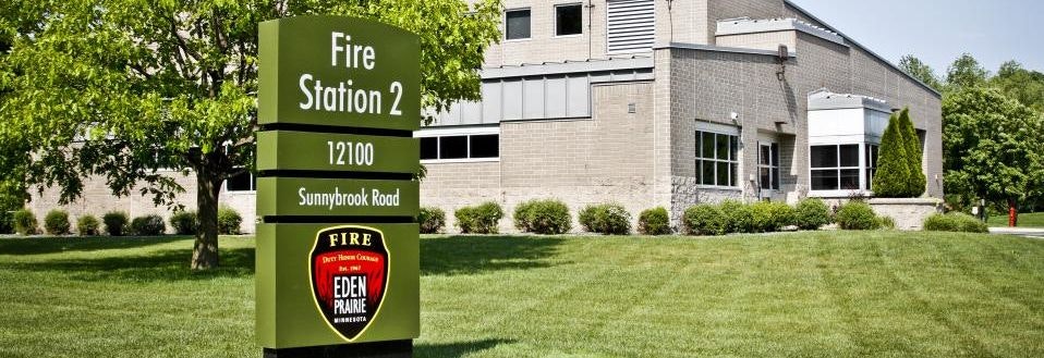 Sign for "Fire Station 2" on a sunny day with well-kept grass and part of the station building in the background.