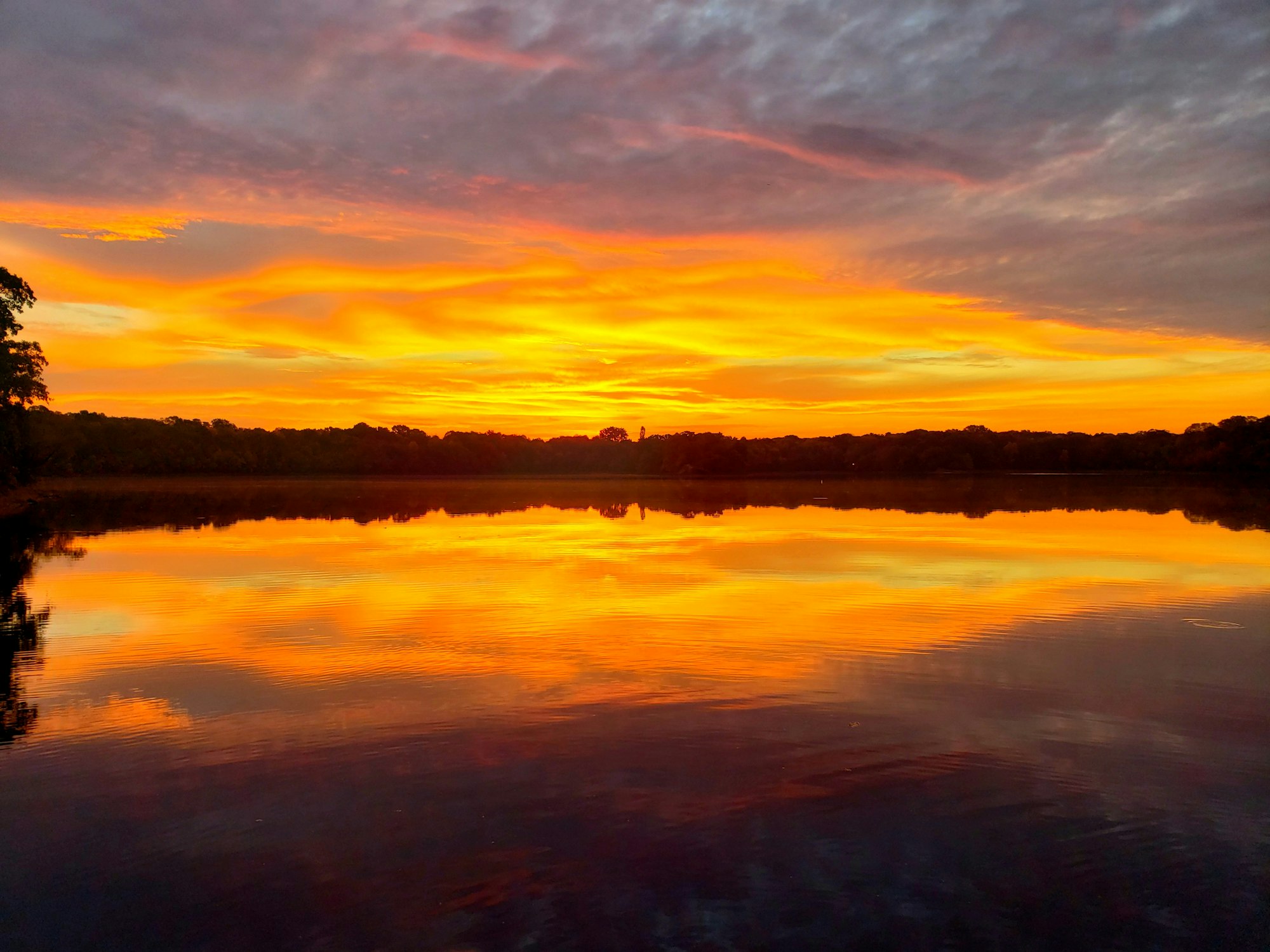 Vibrant sunset with fiery clouds reflected in a tranquil lake.