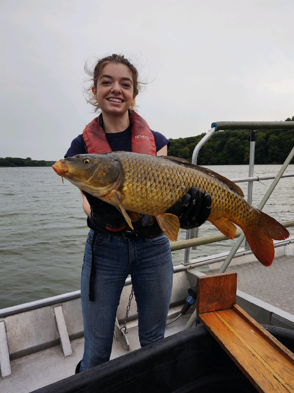 A smiling person on a boat, wearing a life vest, proudly holding a large fish.