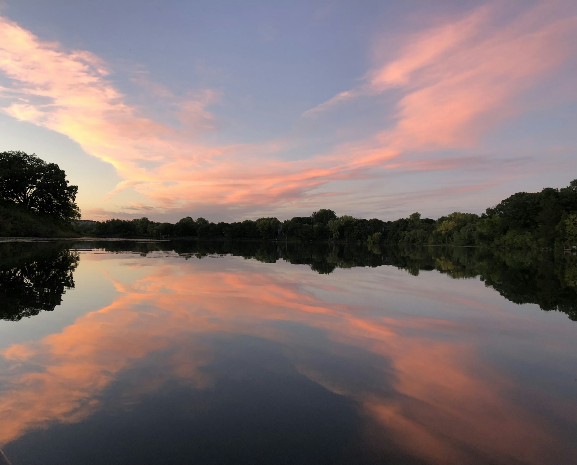 A serene lake reflecting pink-tinged clouds and trees at dusk.