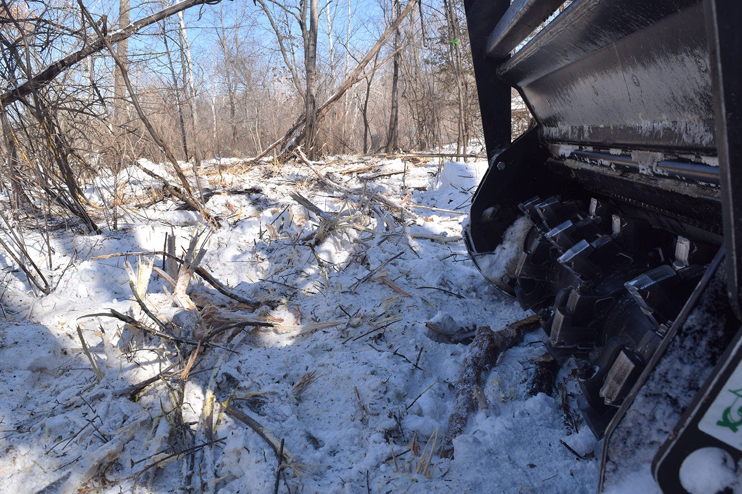 Snowy clearing with twigs, viewed over a machine part.