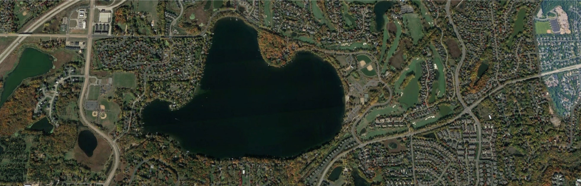 Aerial view of a lake surrounded by residential areas, roads, and green spaces.