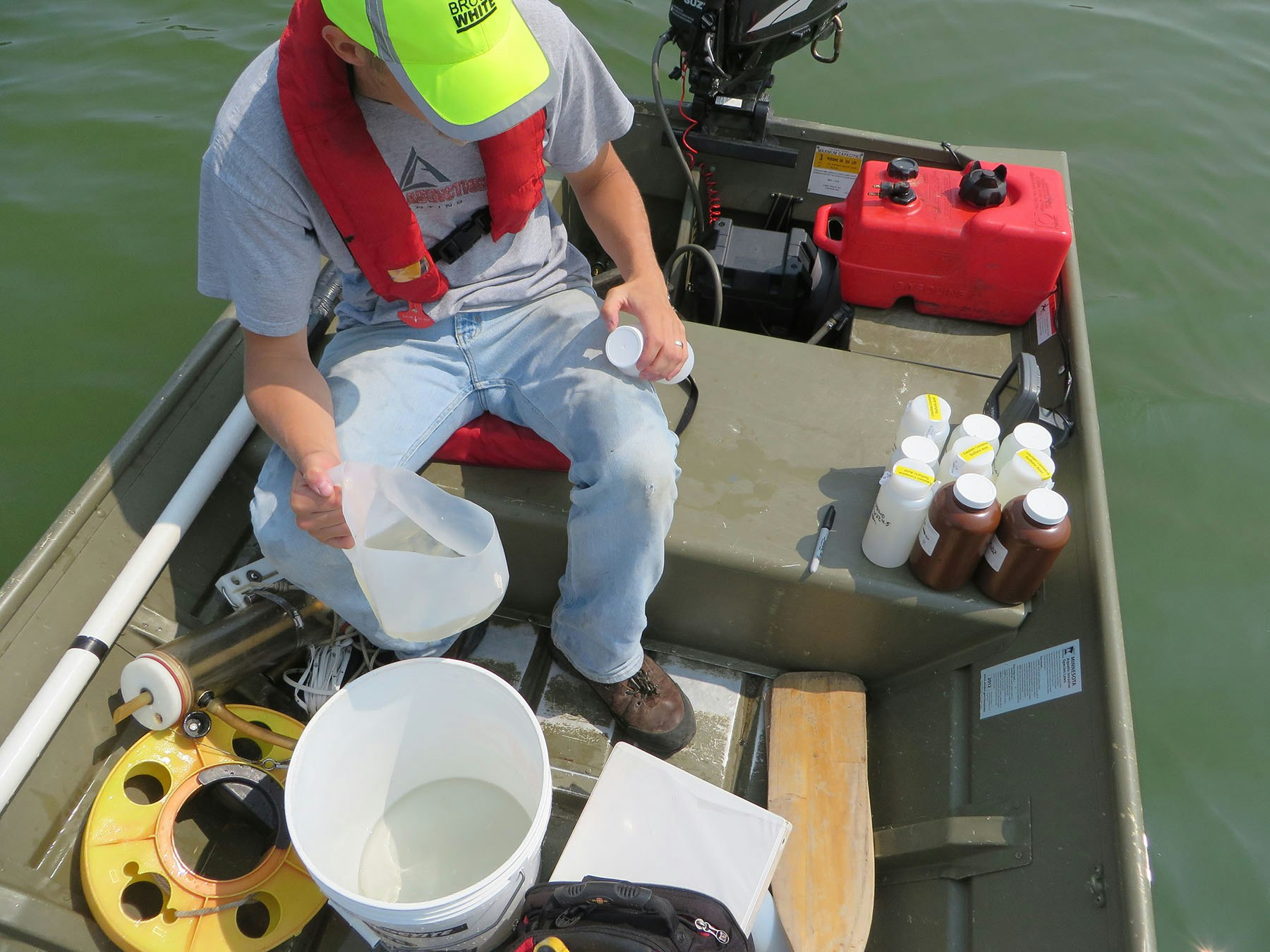 A person sitting in a boat with water samples and scientific equipment.