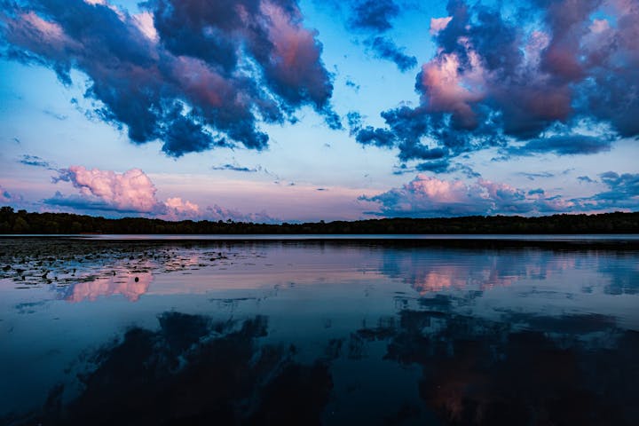 A serene lake reflecting a dramatic sky with fluffy clouds at dusk.