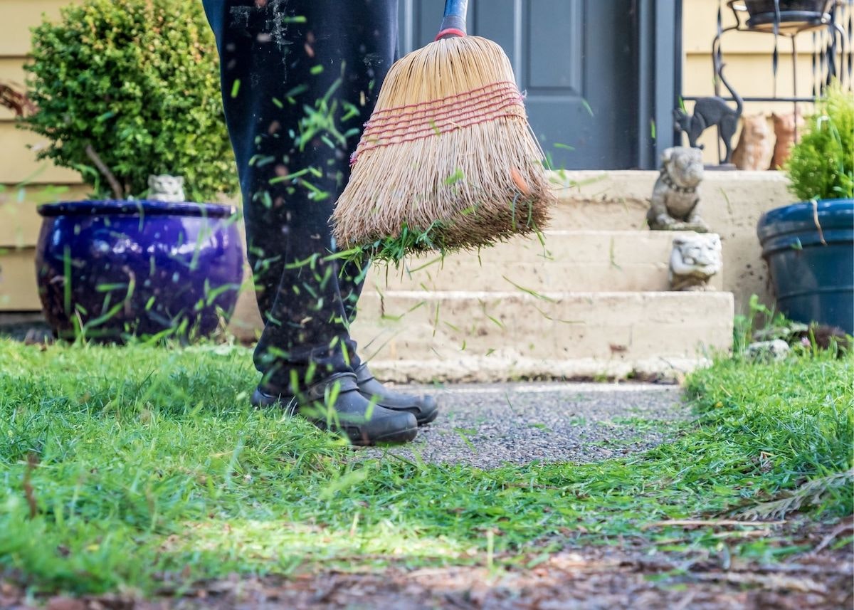 Person sweeping grass clippings with a broom outdoors.