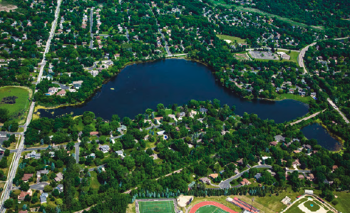 Aerial view of a suburban area with a lake, streets, houses, and sports fields.