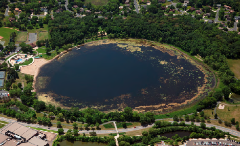Aerial view of a lake with algae bloom, surrounded by greenery and urban development.