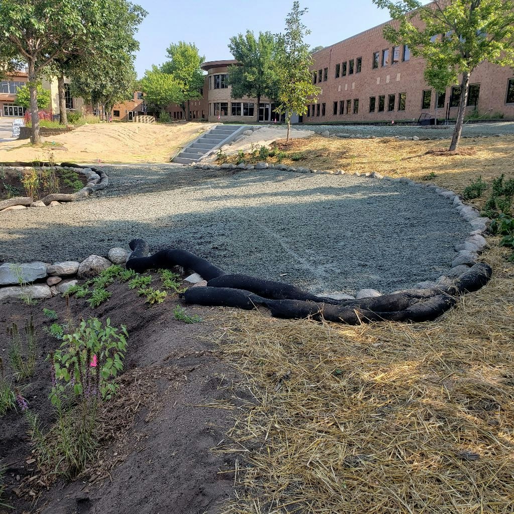 A landscaped area with gravel, rocks, and straw near a building.