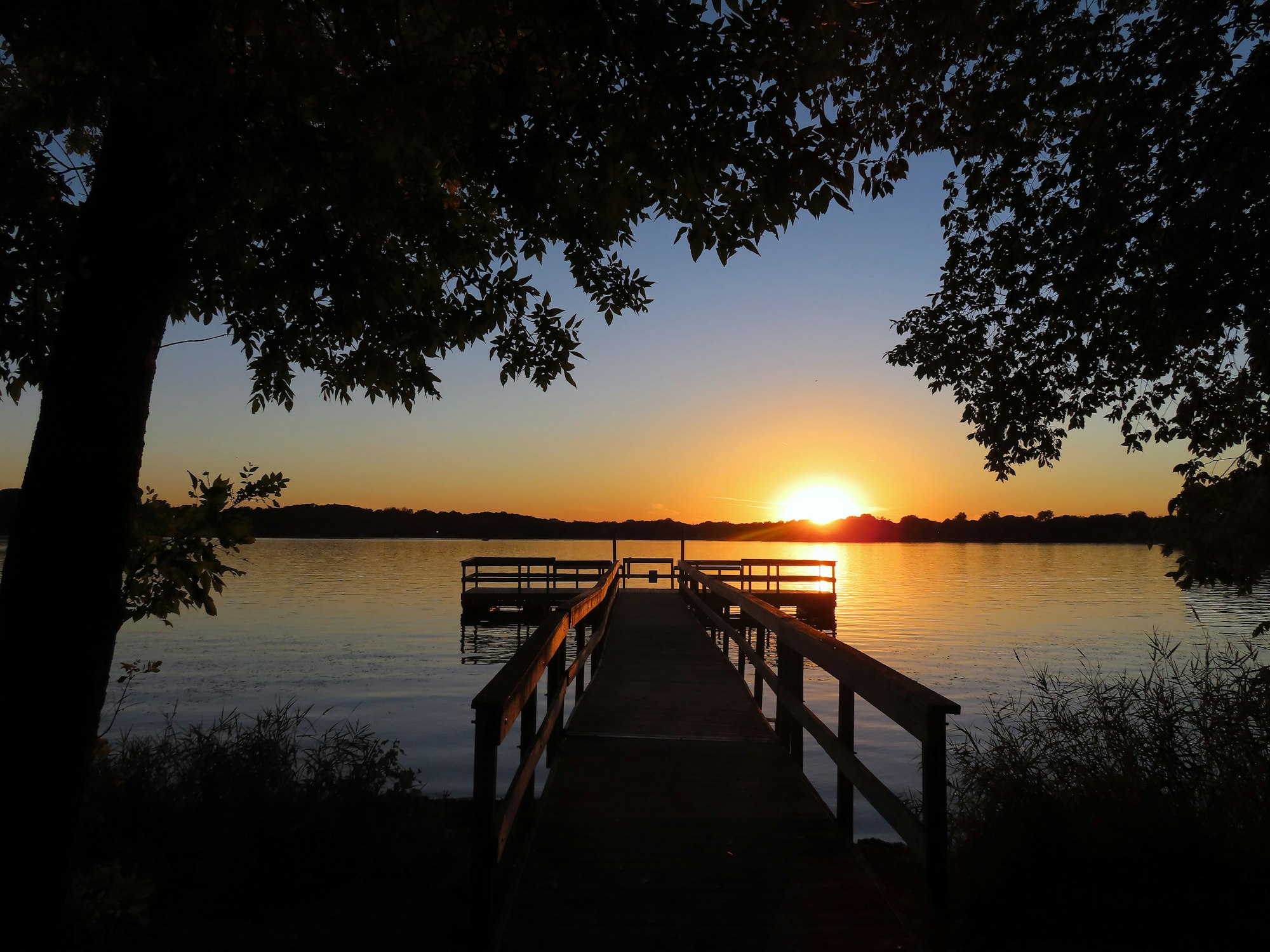 A serene sunset view over a lake with a dock framed by trees.