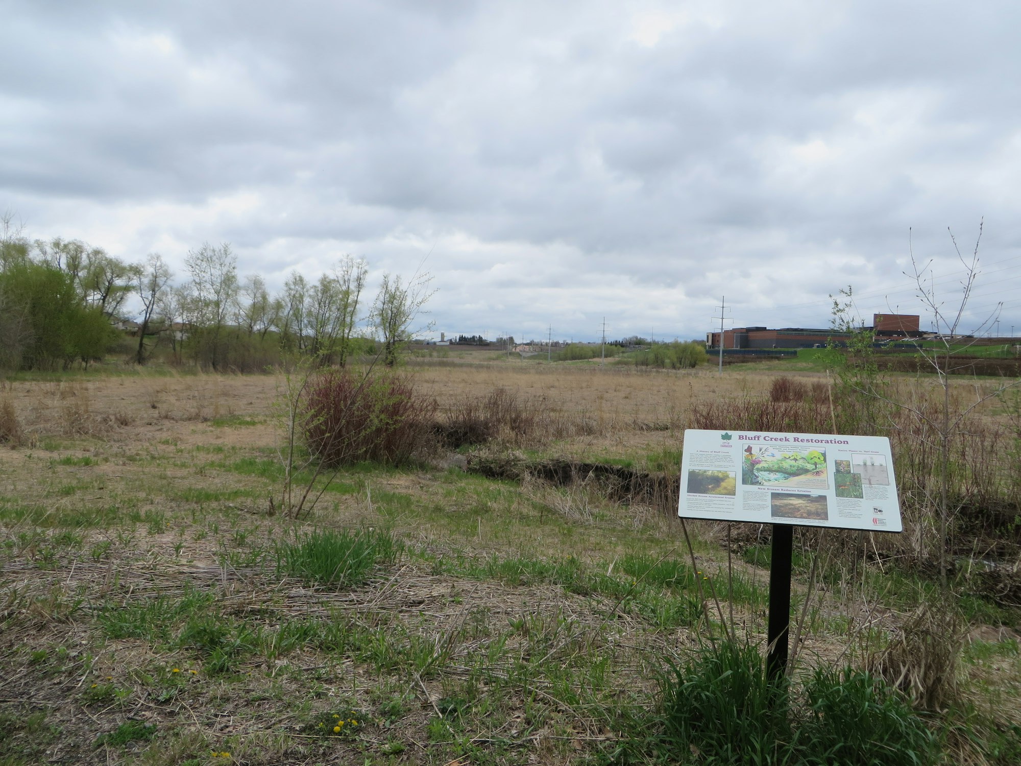 Restoration sign in a field with cloudy skies and distant buildings.