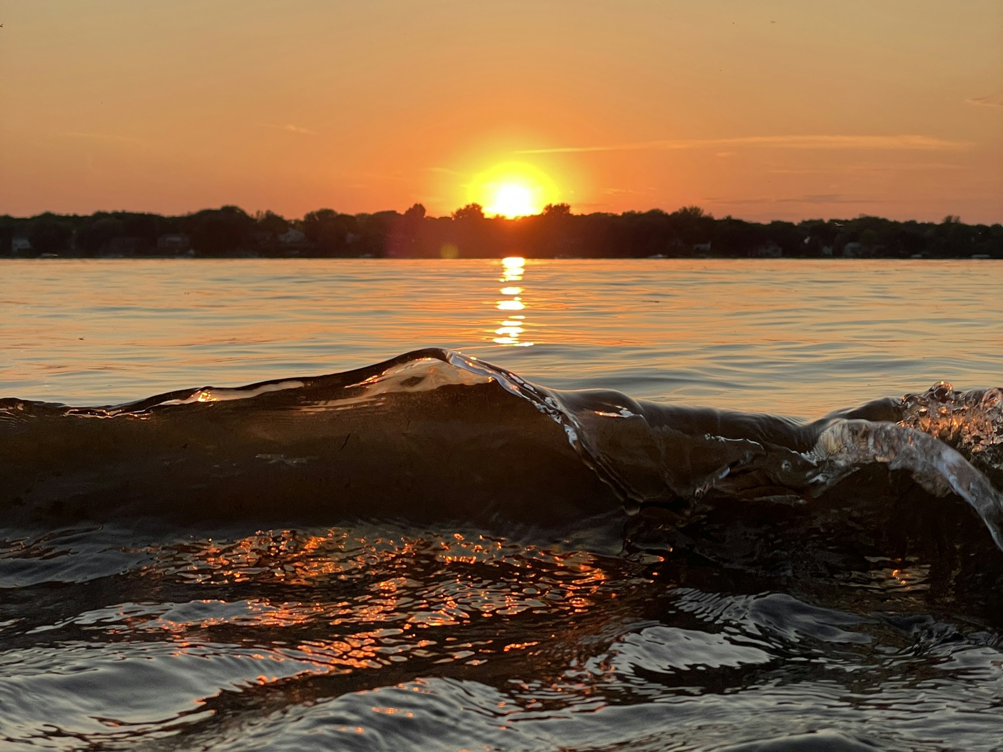 Sunset over water with a close-up of a wave crested by the sun's reflection.
