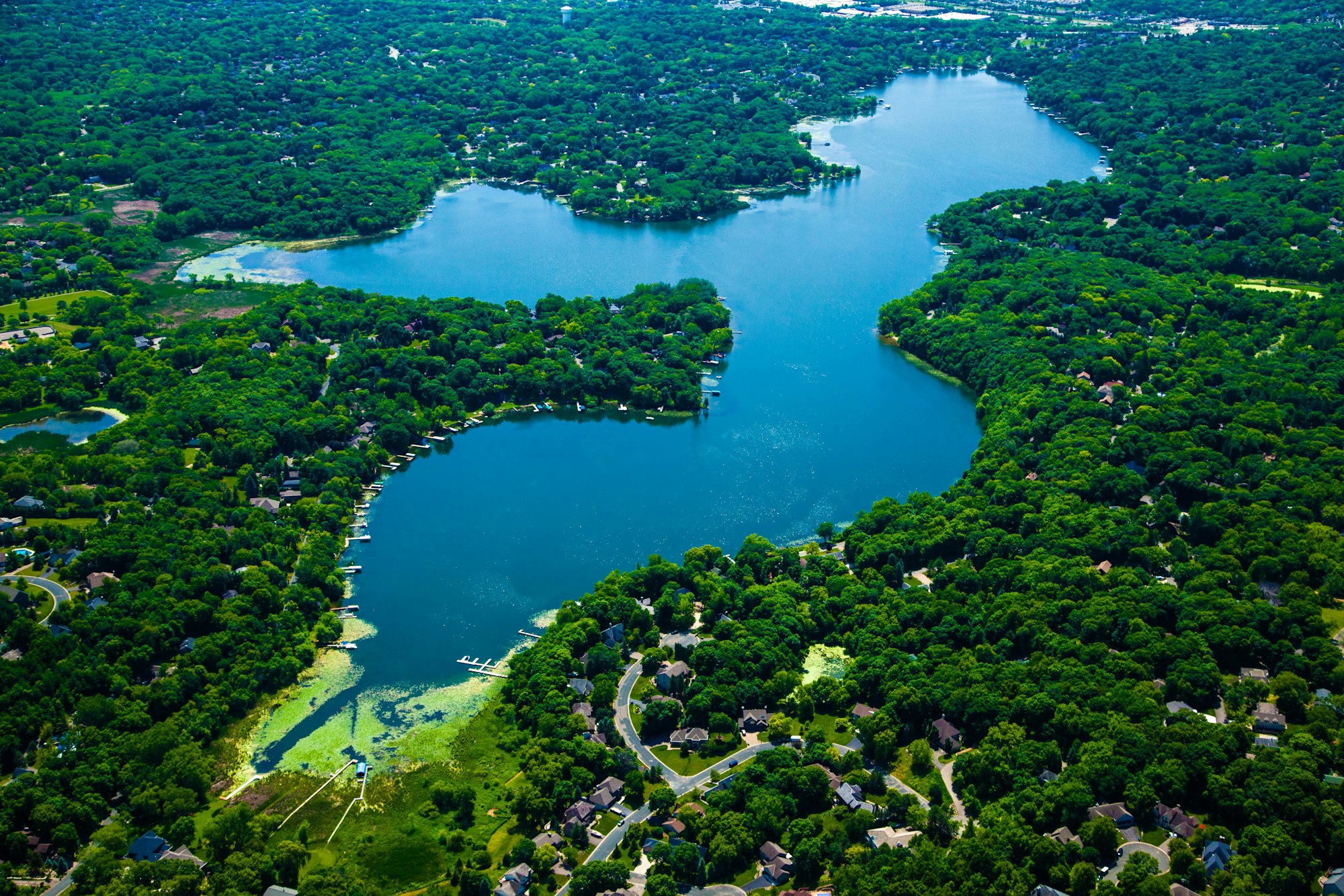 Aerial view of a lush, green landscape with winding rivers and lakes amidst residential areas.