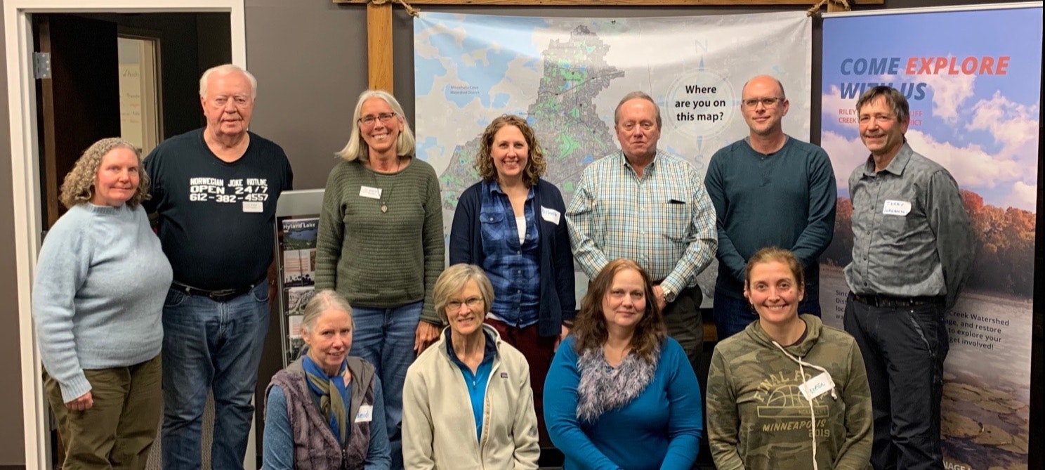 Group of people posing in front of a banner saying "Come Explore With Us" with maps in the background.
