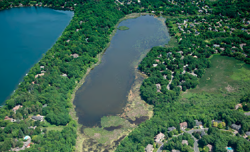 Aerial view of a winding river near a lake with surrounding greenery and residential houses.