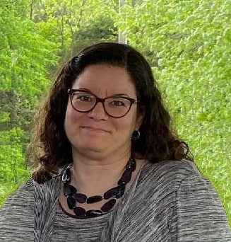 Woman smiling with glasses in front of trees wearing a dress with necklace