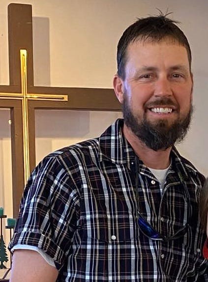 Bearded man in casual collared shirt in front of a cross above an altar