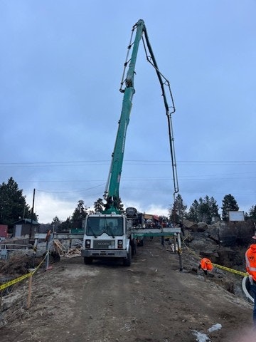 A large concrete pump truck is set up at a construction site, extending its boom towards the sky amid overcast weather.
