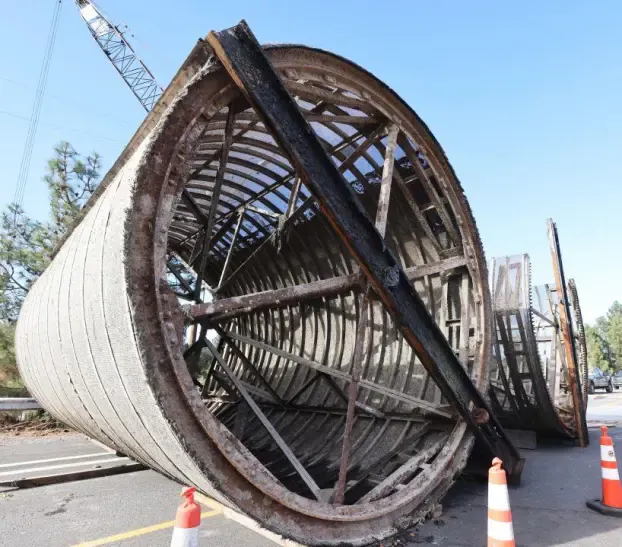 A large, overturned concrete structure lies on the roadside, surrounded by traffic cones and a construction crane in the background.