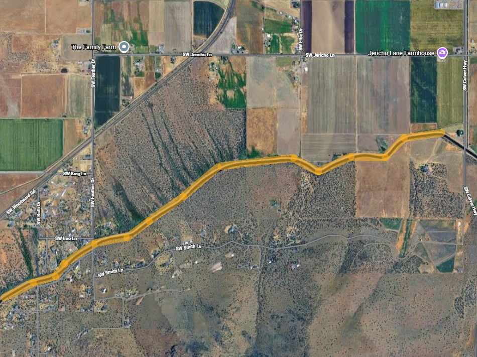 Satellite view of a rural area with fields and farms. A highlighted yellow path runs through, with labeled roads and landmarks.