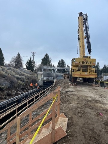 A construction site with a large crane, workers in safety gear, and a partially constructed structure alongside a waterway.