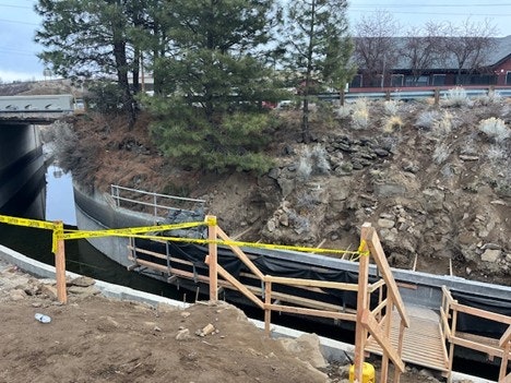An image showing a pathway with wooden stairs, caution tape, and a waterway, likely near a road or highway.