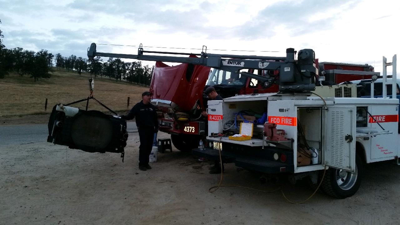 fire engine being repaired by fleet dervices. The boom arm of the repair truck is holding a radiator suspended above the ground