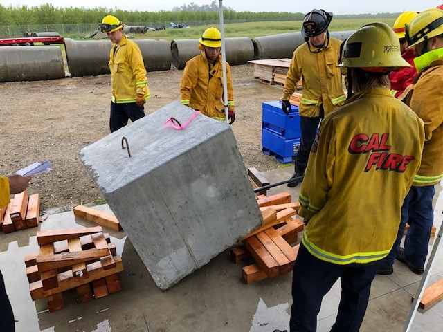 Several fireghters using cribbing to stablize a large cement cube as they practice lifting and rotating the block during a rescue systems one course