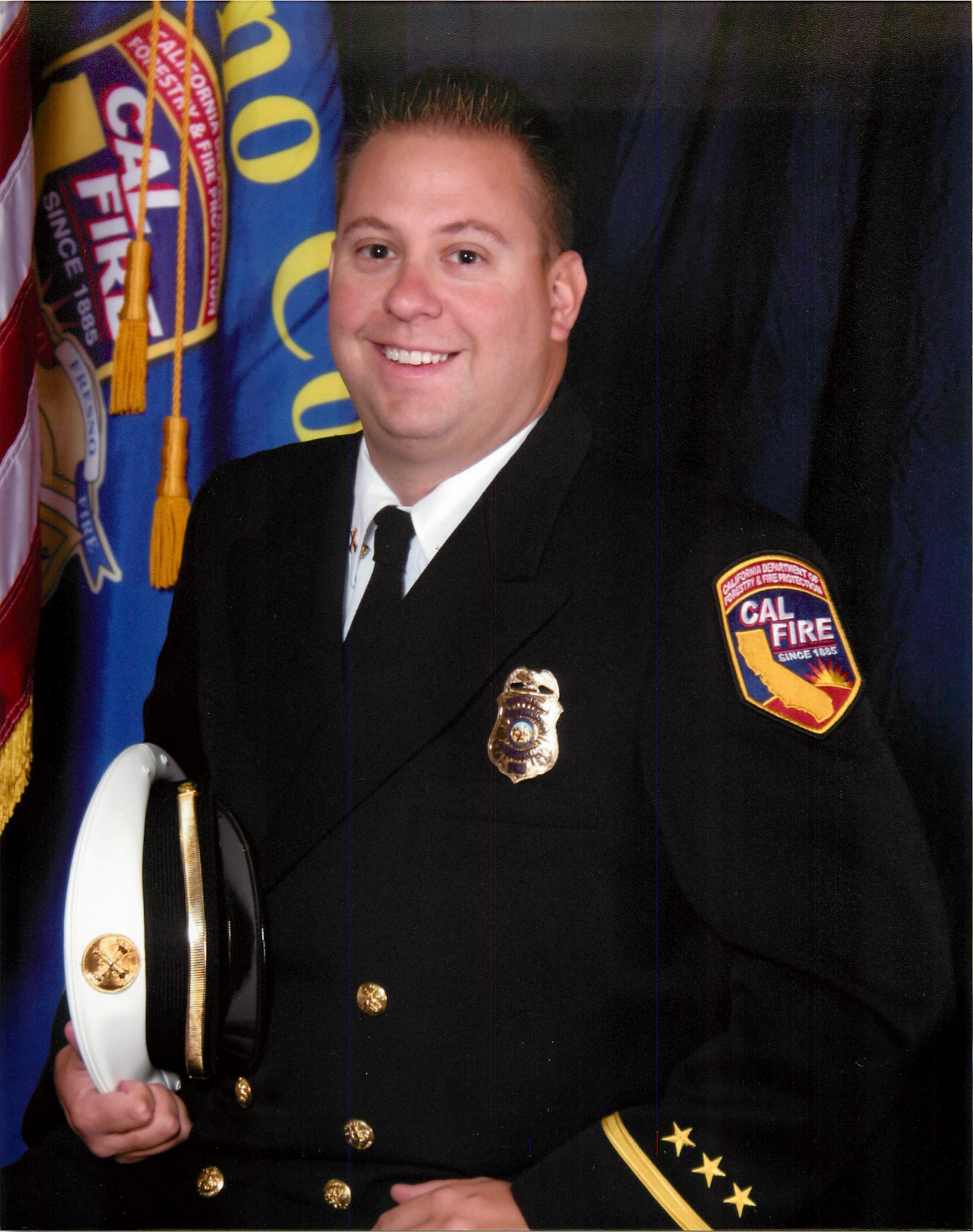 Chief Officer in Class A uniform. American flag and Department flag in background