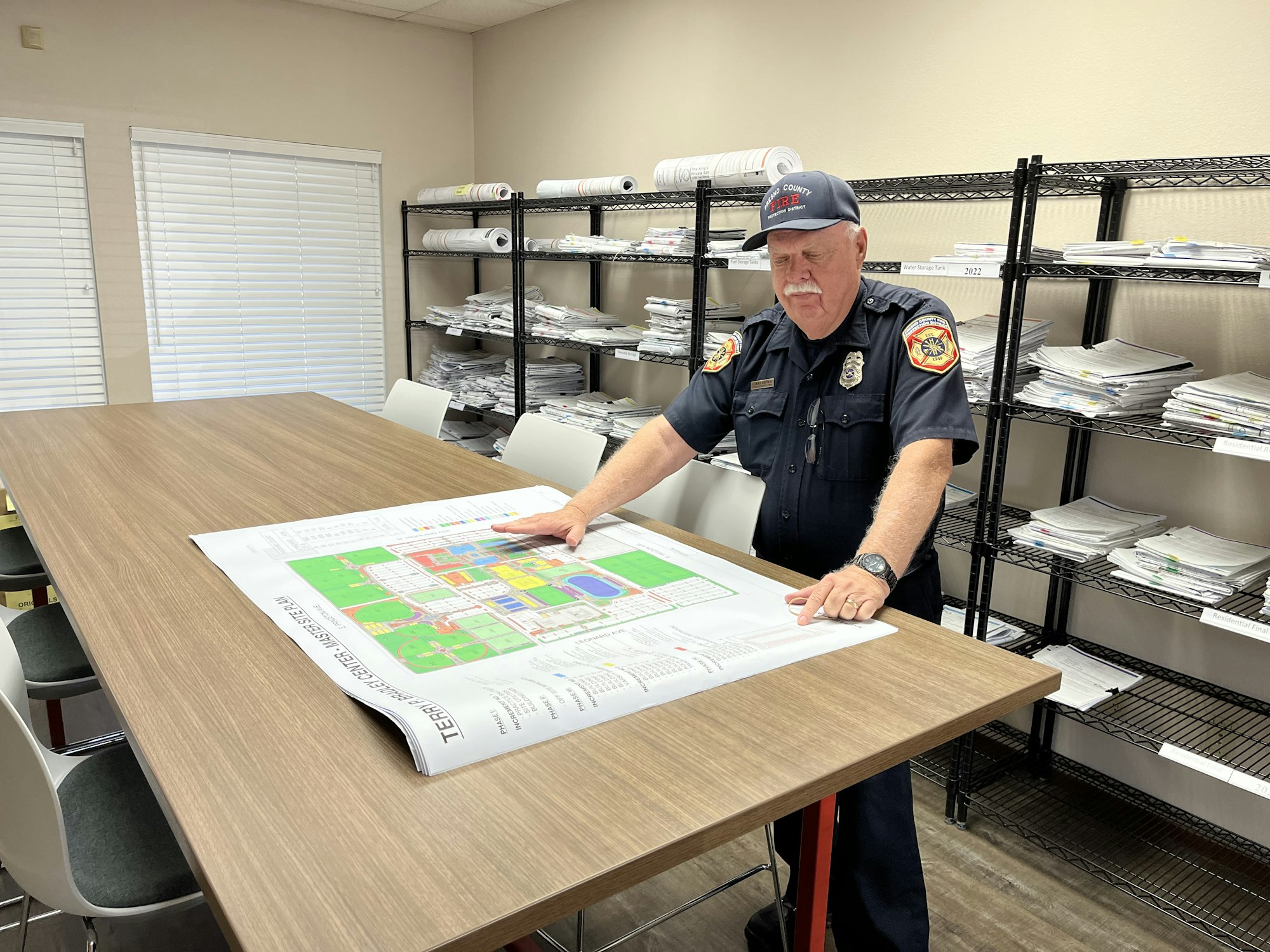 Senior fire inspector reviewing plans on a table with stacks of plans behind him