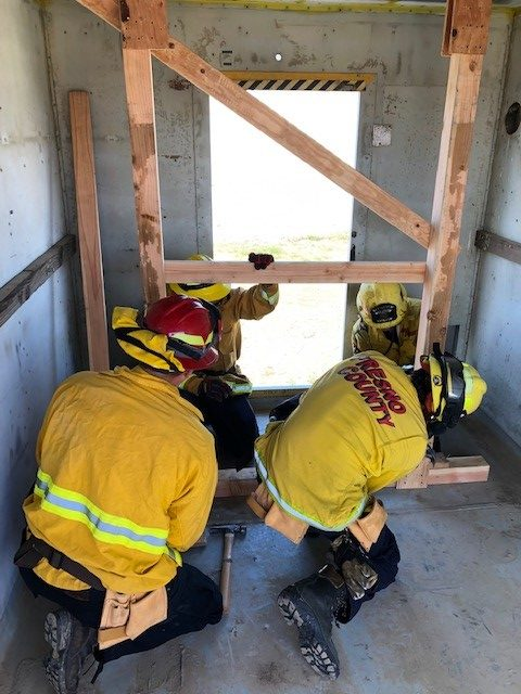 Several fire fighters are using wood shores to stabilize a simulated structural collapse issue in a doorway.