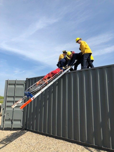 Several firegithers on top of container on the drill grounds with a training victim secured to a stokes using a rescue systems 1 technique called moving ladder slide