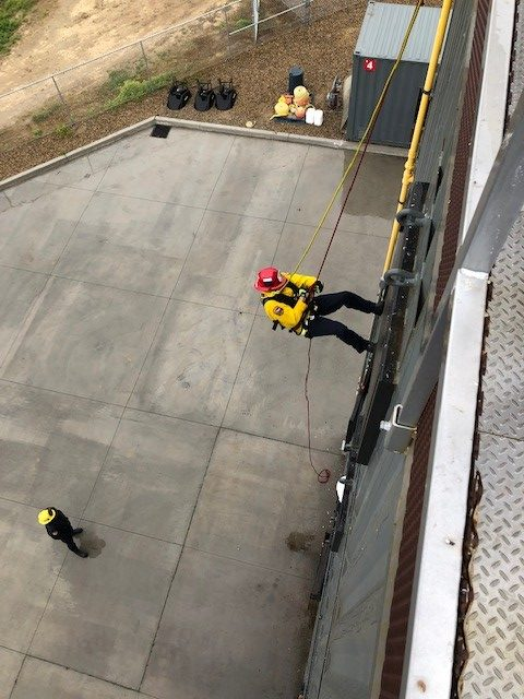 a firefighter is being lowered on the tower and is shown mid decent 30' in the air