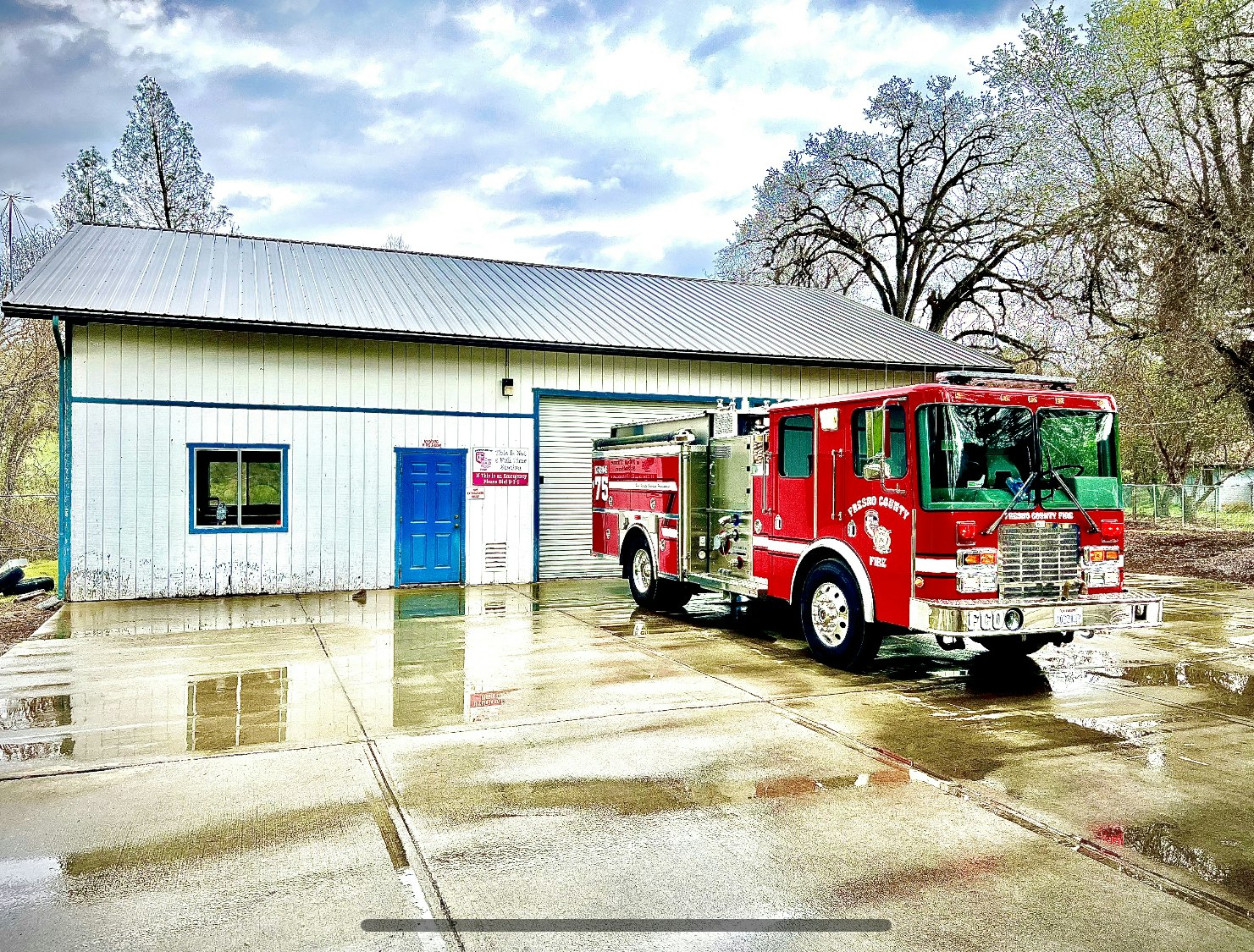 fire truck parked on wet pavement in front of metal apparatus bay