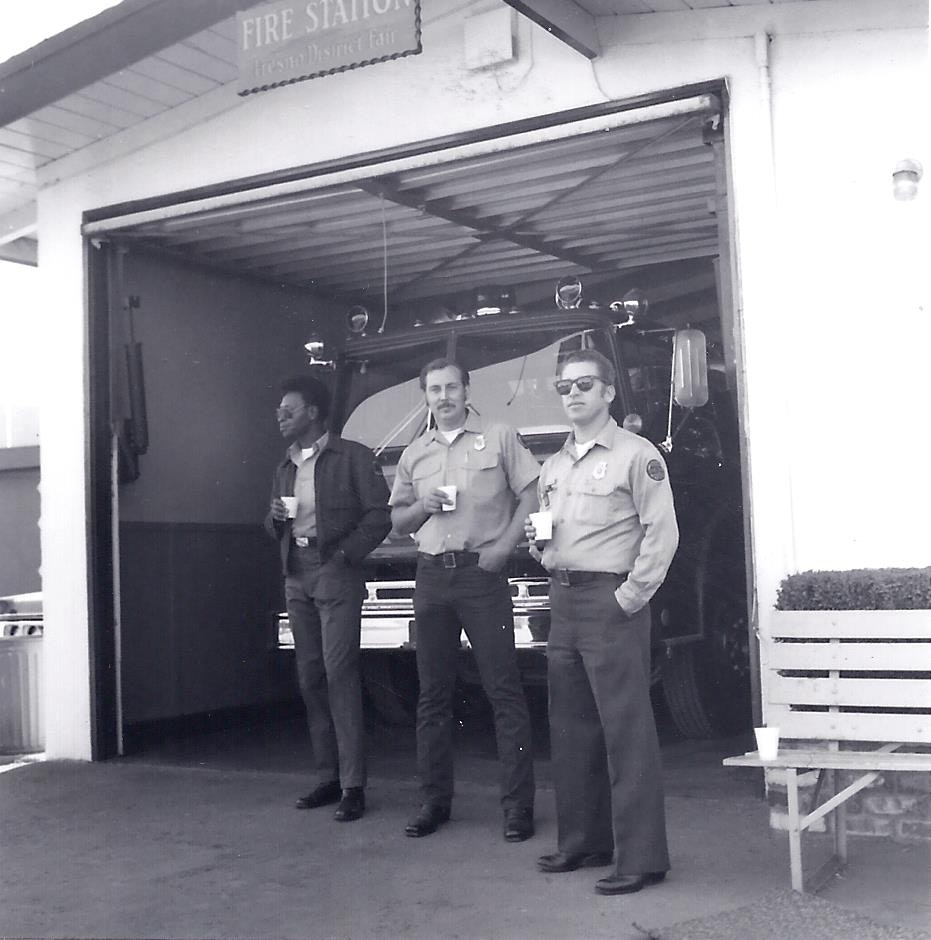 black and white picture of the 3 member crew having coffee in front of the facility standing in full uniform