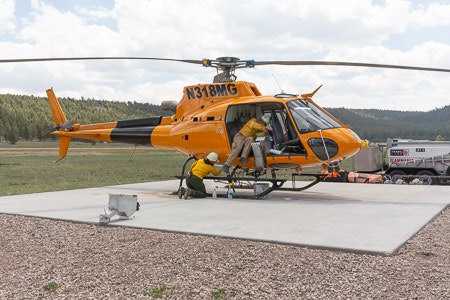 A yellow helicopter on a pad with a person wearing a helmet standing beside it.
