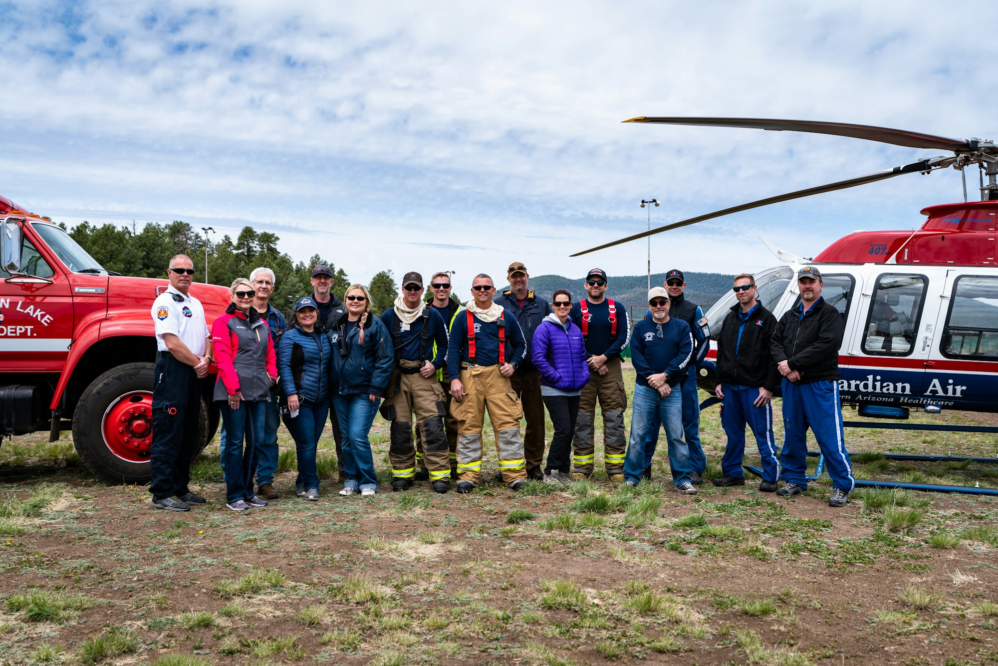 Group of people in front of a fire truck & helicopter, likely emergency responders or a rescue team.