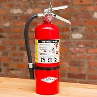 A red fire extinguisher with label and instructions, against a brick wall background.
