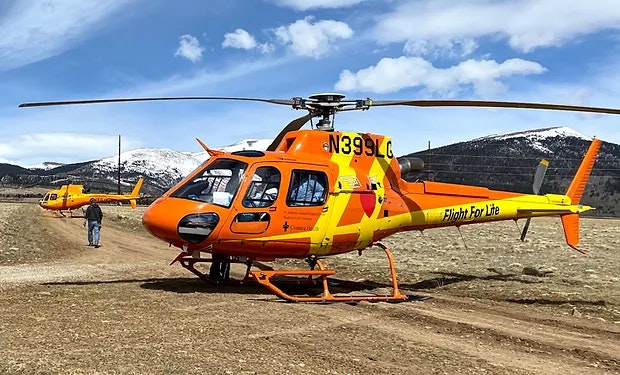 Orange medical helicopters with "Flight For Life" text, mountain background, and person in high-visibility clothing.
