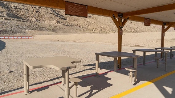 A spacious, covered outdoor area with several empty tables, overlooking a dusty landscape and mountains in the background.