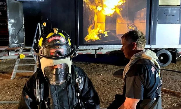 Firefighter in gear with flames in background.