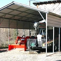 A red tractor parked under a metal shed next to a wooden building.