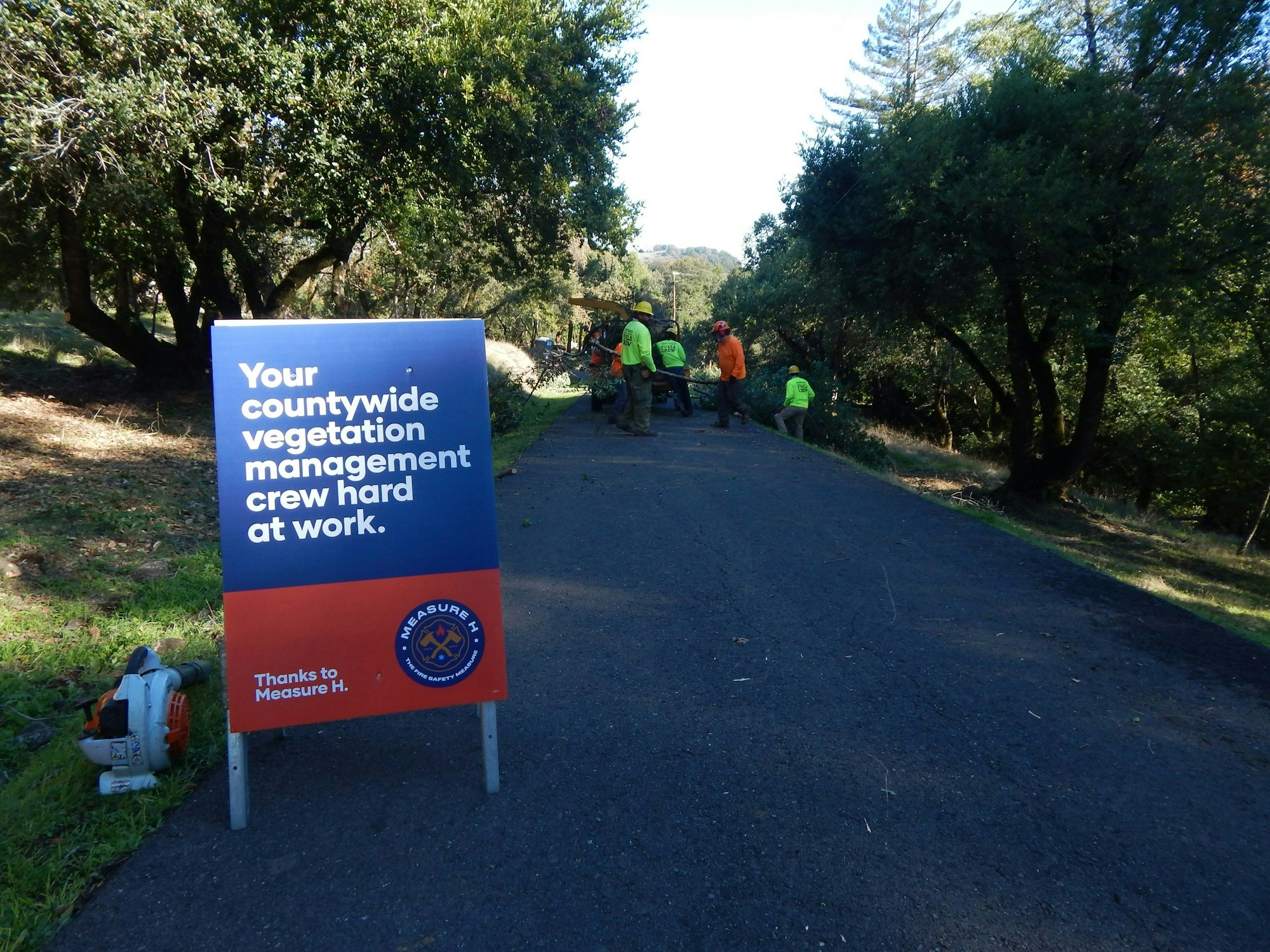 A sign announces a vegetation management crew at work, with team members seen clearing the area in a natural setting.