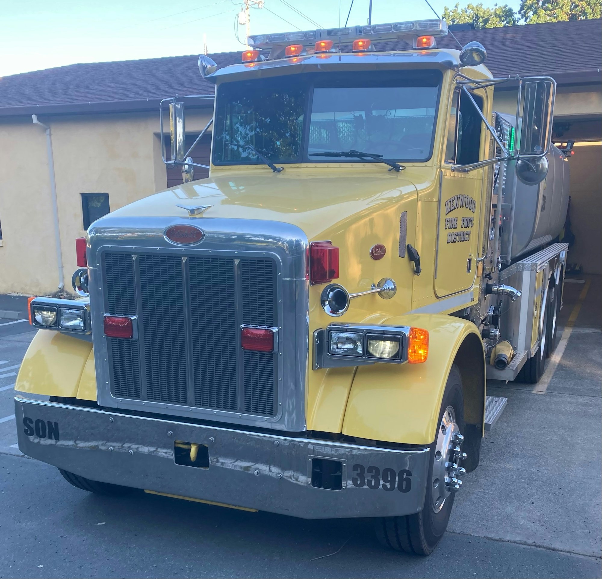 A yellow fire truck with a water tank is parked near a building.